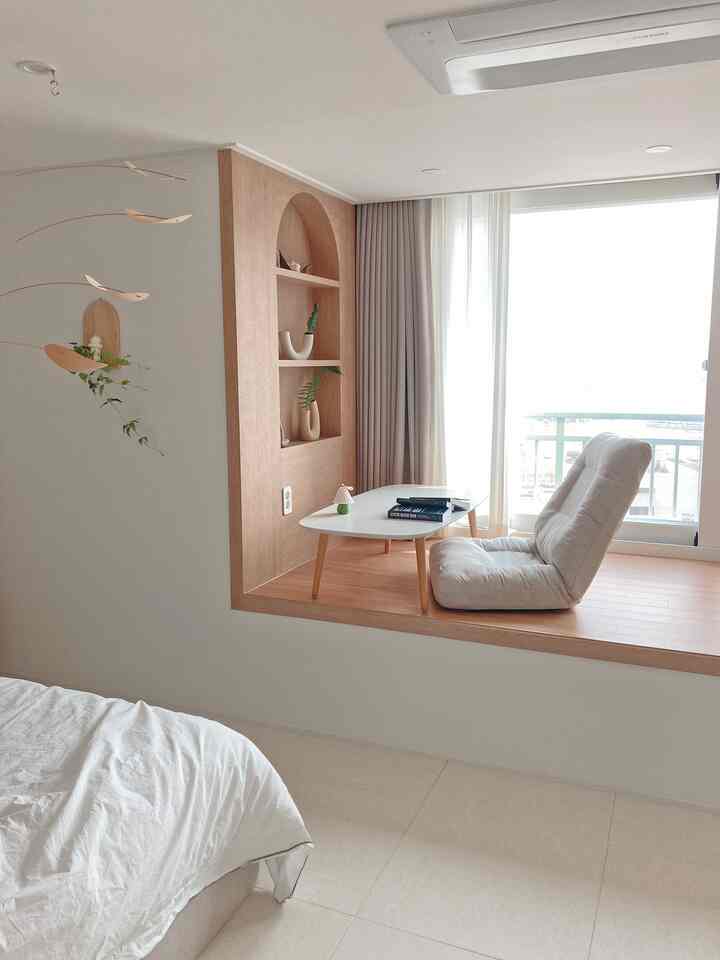 Bright white and wood-tone bedroom with raised floor featuring a single low sofa and blackout curtains for a cozy master room