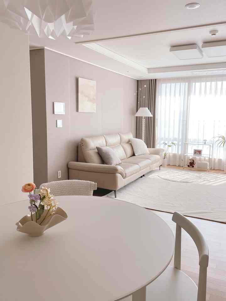 ベージュとホワイトの色調のリビング、ベージュのソファと丸いダイニングテーブルに置かれた花瓶が調和したナチュラルモダンなインテリア