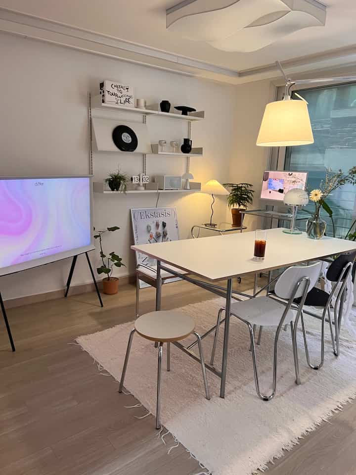 A white and wood-toned living and dining room featuring a modern table, chairs, lighting, and plants creating a cozy atmosphere