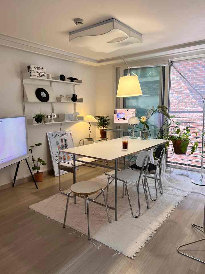 ホワイトとウッドトーンが調和したリビング、中央にダイニングテーブルと椅子が配置され、さまざまな照明と植物がある雰囲気のあるインテリア