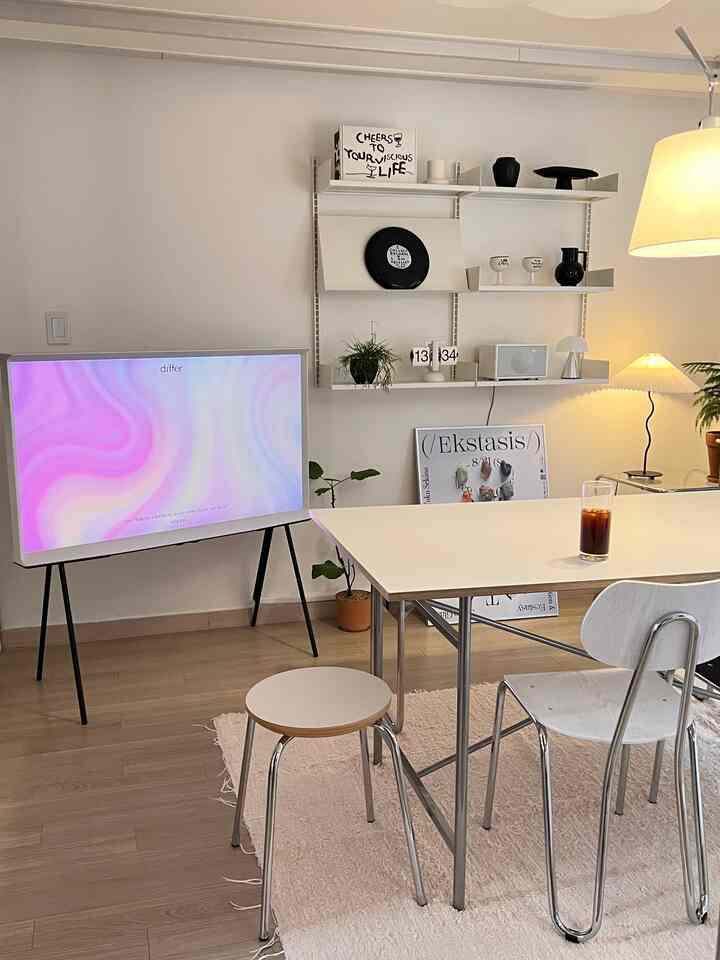 Minimalist living room in white and beige tones featuring a white dining table, chairs, wall shelves, and lamps creating a clean atmosphere