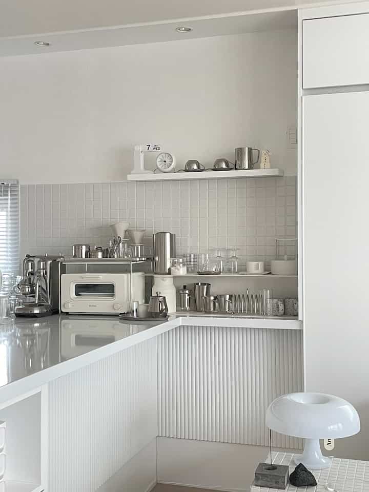 白とシルバーのトーンで統一されたミニマルなキッチン、壁の棚にコーヒー用品が整然と配置されたおうちカフェの雰囲気