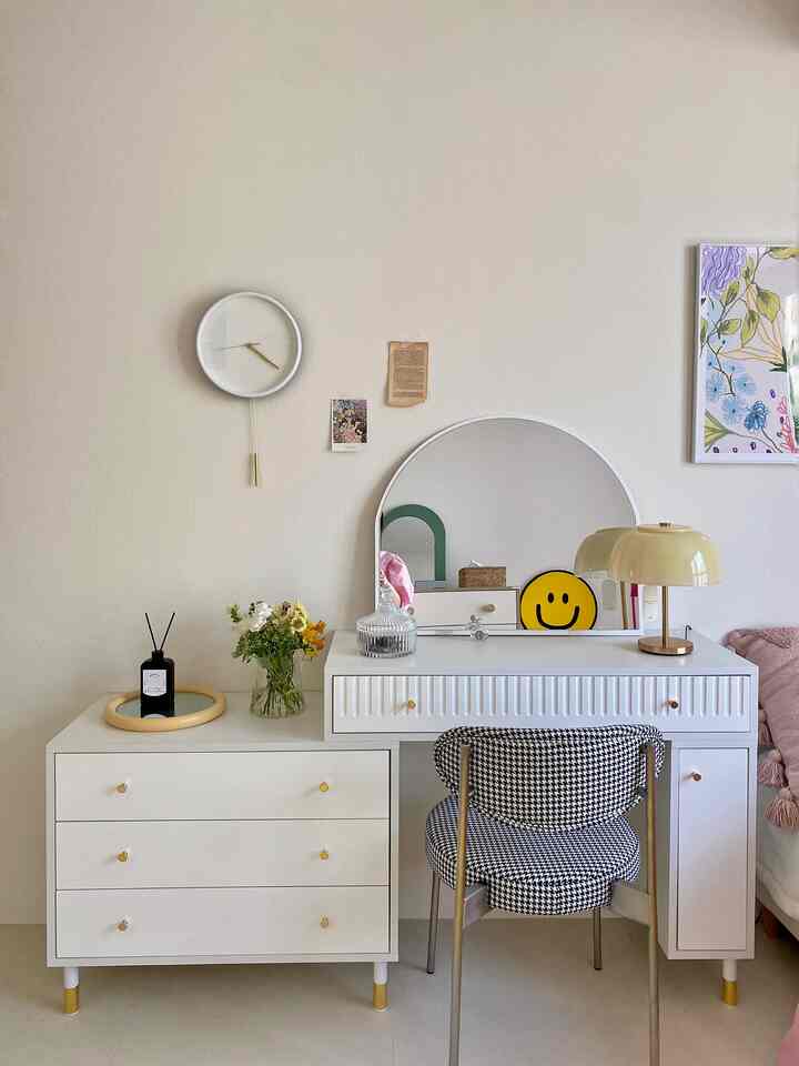 Beige and white toned bedroom vanity area featuring a silent wall clock and table lamp in a simple modern interior