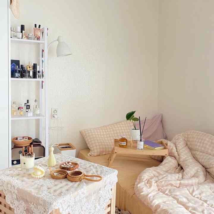 Cozy small beige-toned bedroom featuring a bed, wooden table tray, and white shelving unit for storage