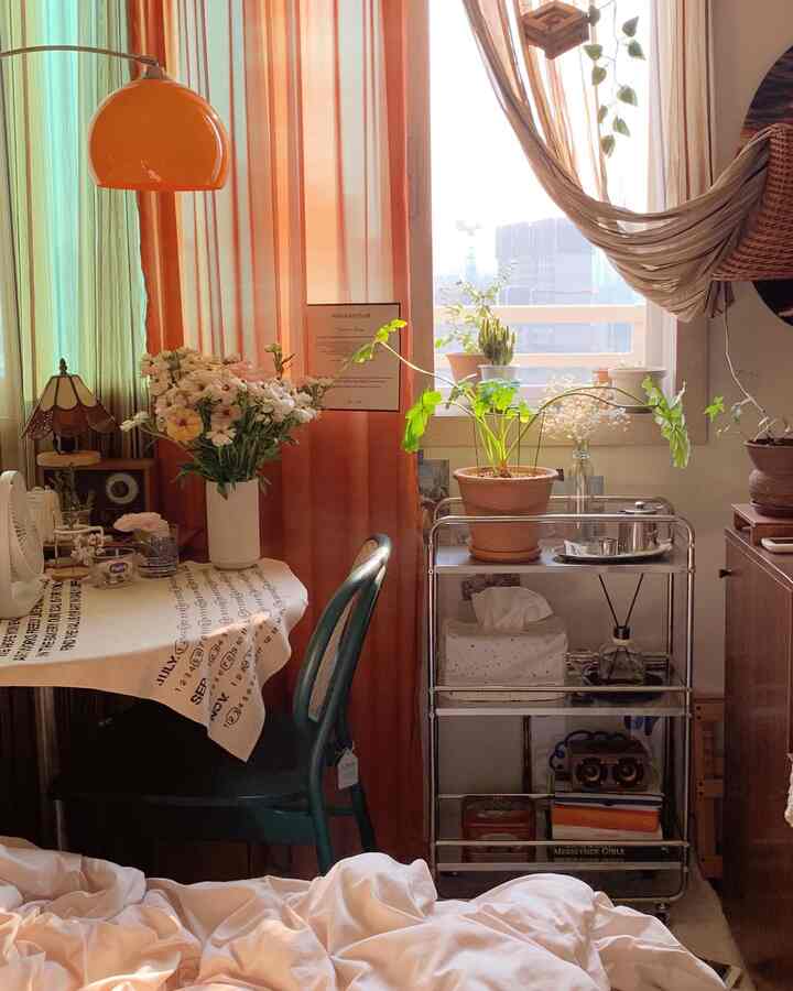 Warm orange-toned curtains and vintage furniture with various plants in a cozy studio apartment space