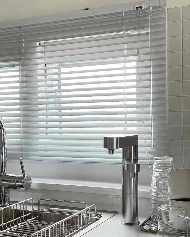 White and silver-toned kitchen featuring aluminum blinds on the window creating a clean ambiance