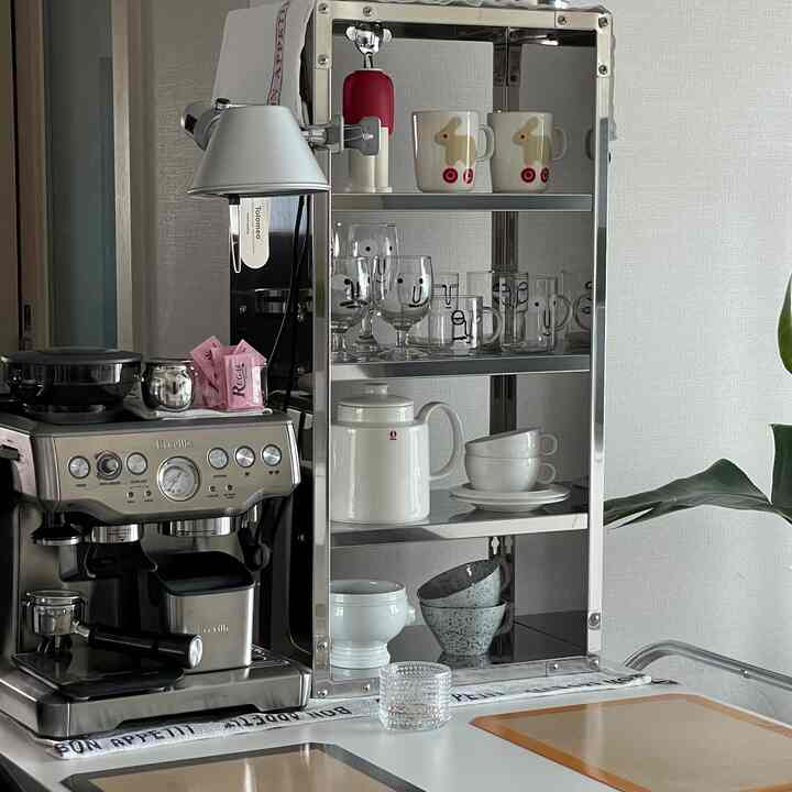 シルバーとホワイトの色調のキッチン、コーヒーマシンや調理器具、棚に並んだカップやティーカップが配置された雰囲気のあるホームカフェ