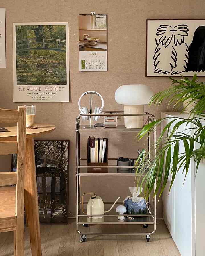 ベージュ色の壁と木目調家具がある空間に、ステンレス製の移動式ワゴンとグリーンプラントが配置されたミッドセンチュリーモダンのインテリア。