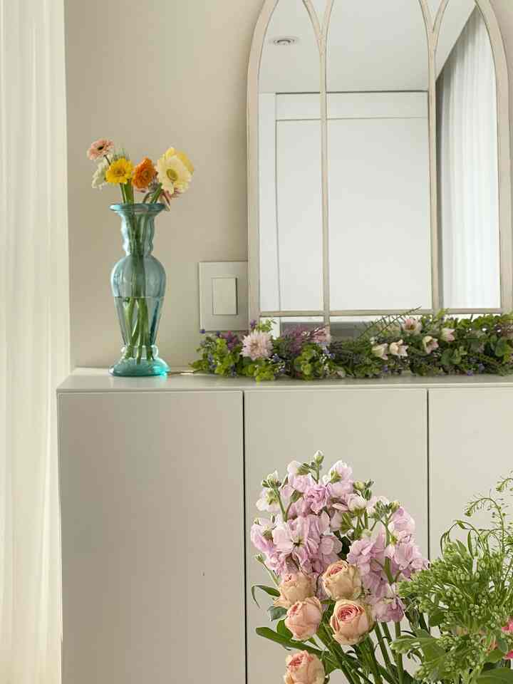 Entrance space in white and beige tones featuring a shoe cabinet with mirror and plant stand, evoking a natural atmosphere