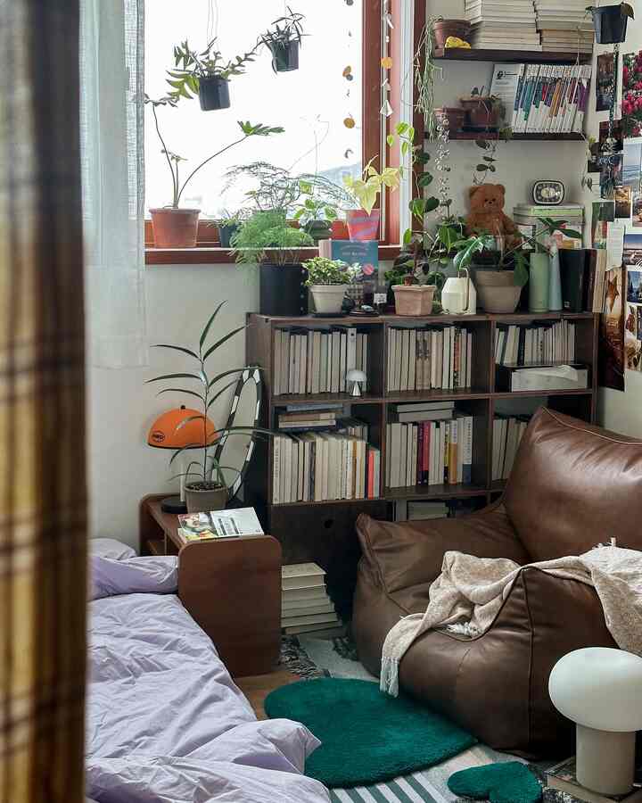 Cozy narrow bedroom with dominant brown and beige tones featuring plants on window sill and bookshelf filled with books