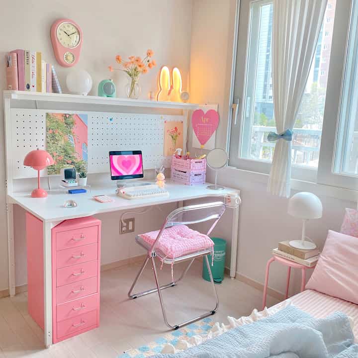 Bright white and pink toned small room featuring a pink drawer desk with computer near window, cozy atmosphere