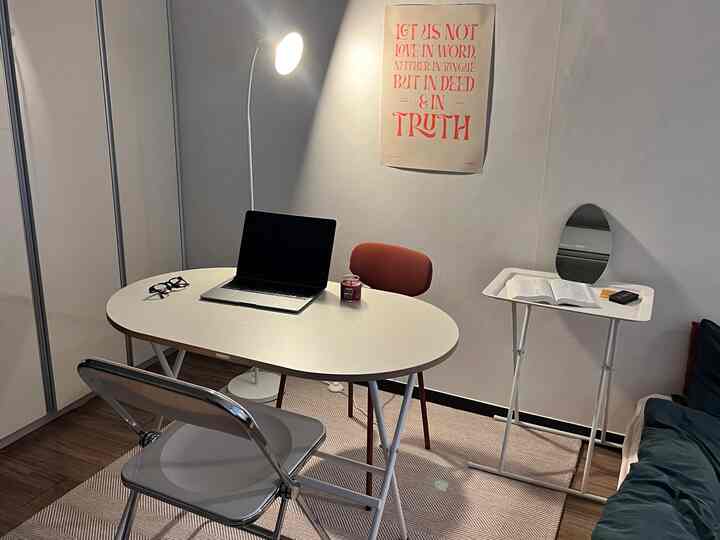 A white-toned living room and home office featuring a white desk, chairs, rug, and an orange poster creating a cozy workspace