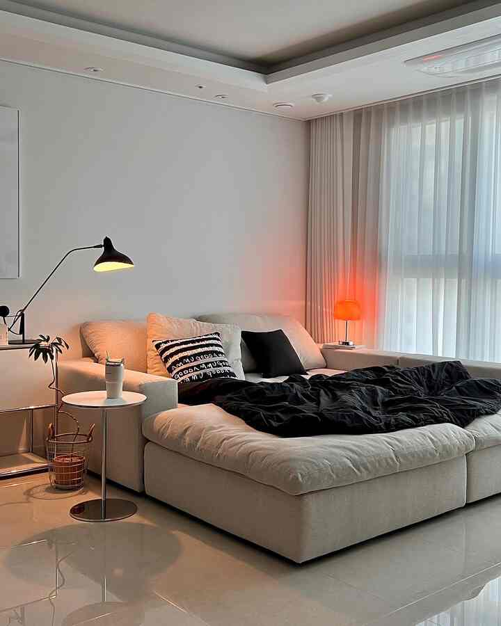 A natural modern living room in white and cream tones, featuring a large cream sofa with black cushions and red table lamp accents