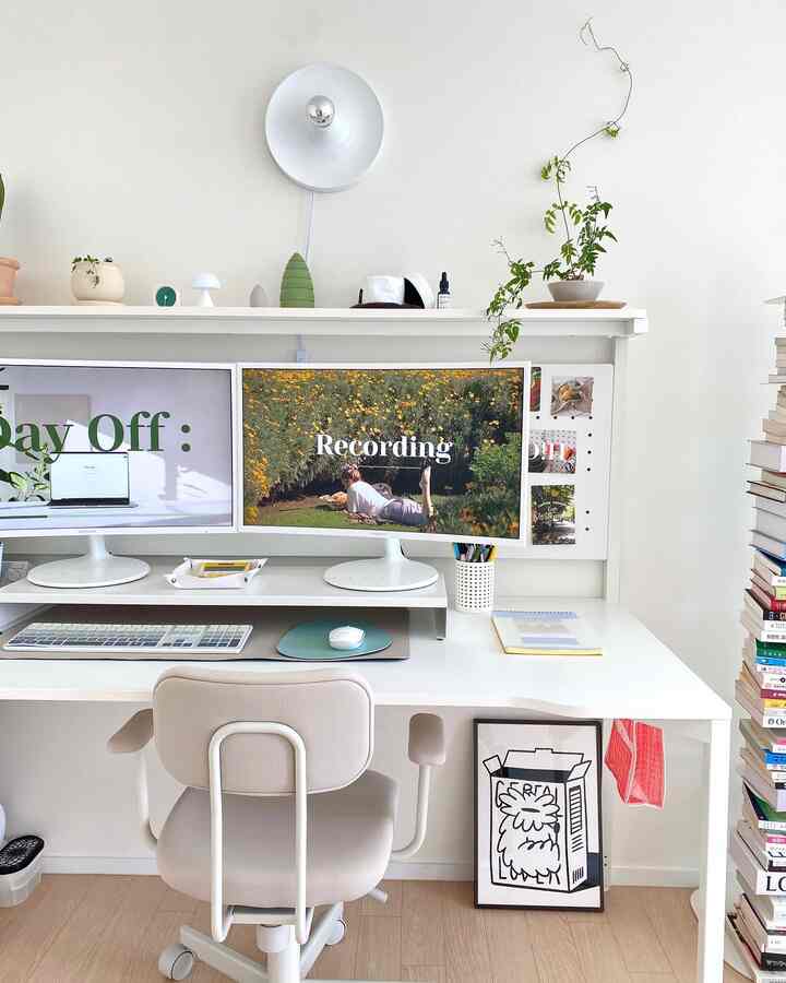 White and natural-toned home office space featuring dual monitors, plants, desk, and office chair in a clean workspace