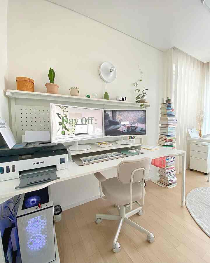 Bright white and light brown toned compact home office featuring a modern desk and office chair, dual monitors, and a tall book stack with clean aesthetic