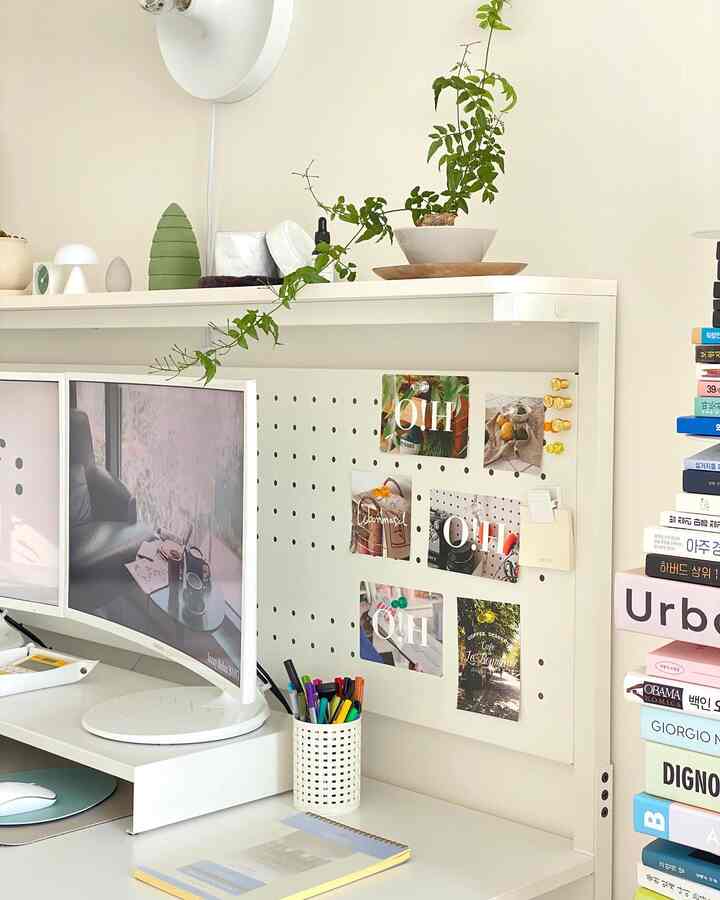 White-toned home office featuring dual monitors on desk with an organized pegboard, creating a clean compact workspace