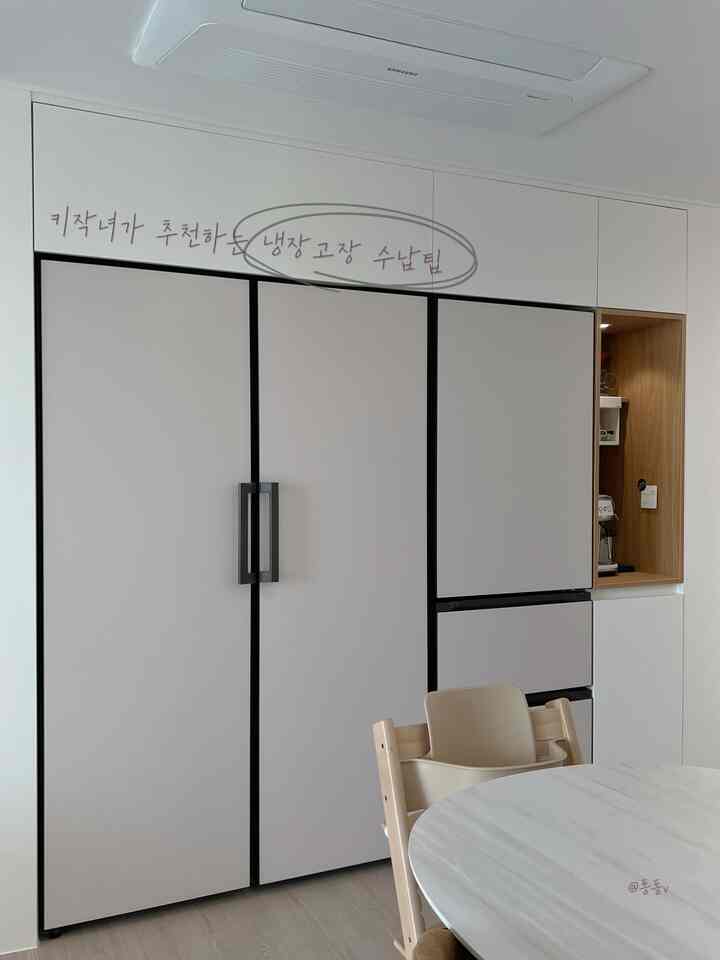 A clean kitchen space in white and beige tones featuring a refrigerator cabinet and a stool focused on storage solutions