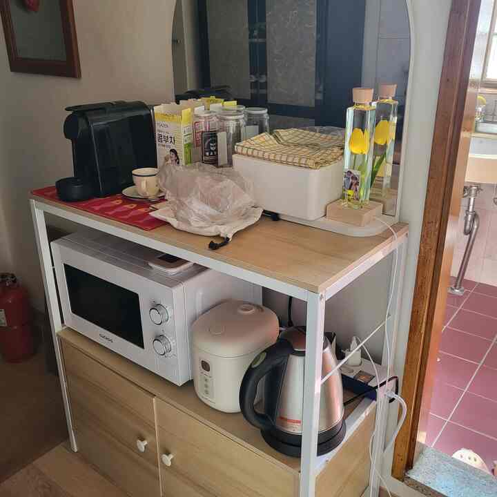 Kitchen space with white and wood tones featuring a microwave, rice cooker, and other appliances neatly organized on storage shelves