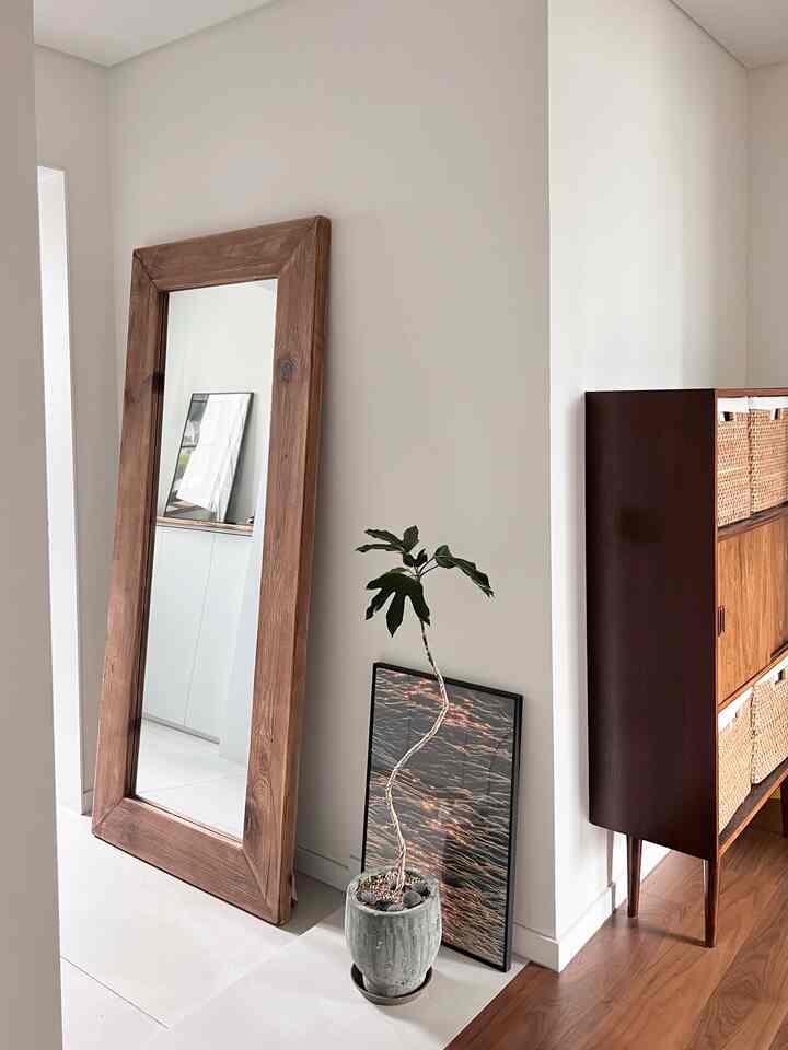 Natural toned entrance space featuring large wood frame full-length mirror and a plant with cozy ambiance