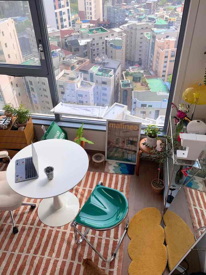 明るいベージュとオレンジの色調のワンルームホームオフィス、丸テーブルとスツール、多様な植物が配置された雰囲気のあるインテリア