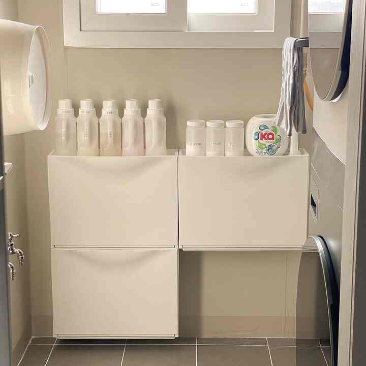 White-toned compact and tidy laundry room featuring a central IKEA TRONES shoe cabinet organized with laundry supplies