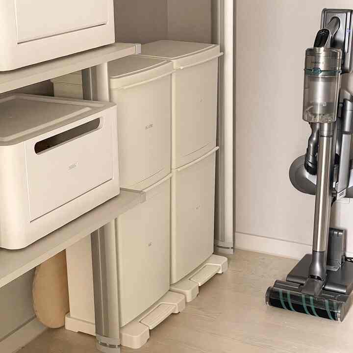 Off-white toned pantry entrance featuring neatly arranged recycling bins, a hanging wire shelf, and vacuum cleaning tools in a tidy utility space