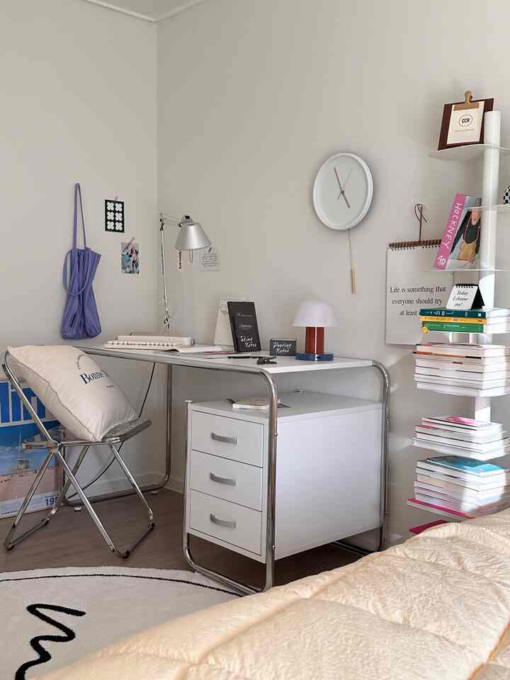 A white and beige toned bedroom and home office space featuring a minimalist white desk and folding chair with a calm atmosphere