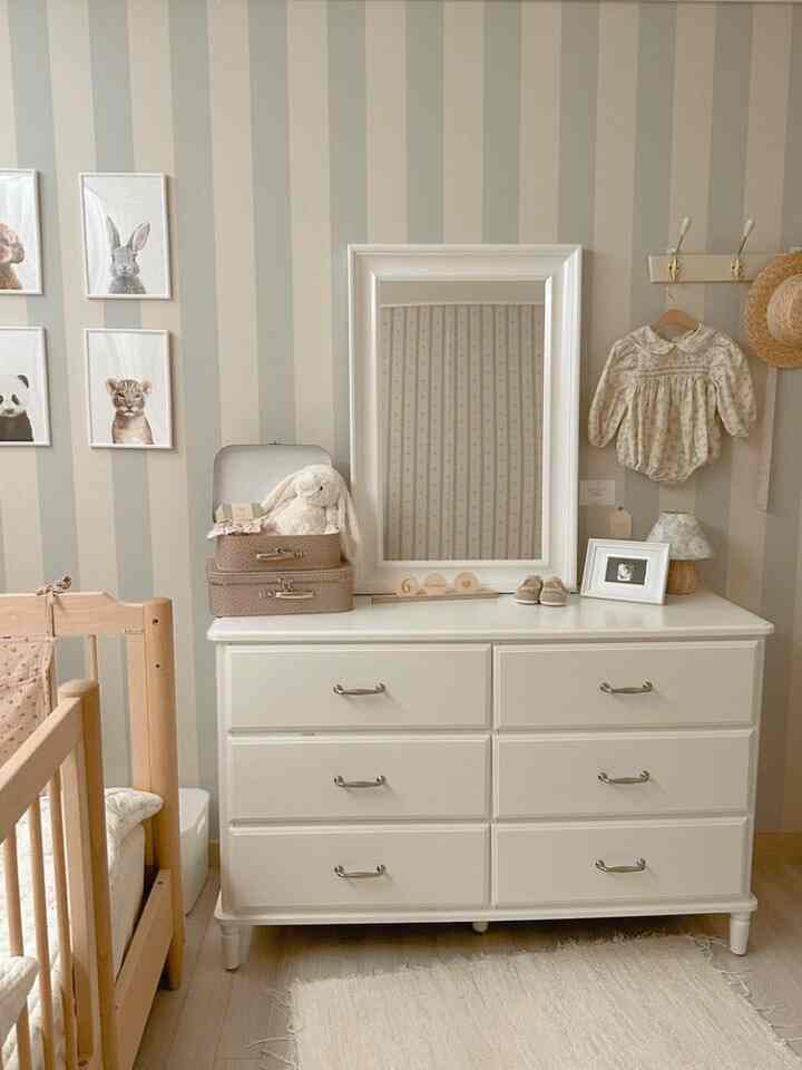 Beige and white toned baby room featuring natural wood crib, white dresser, and animal framed pictures with a cozy atmosphere