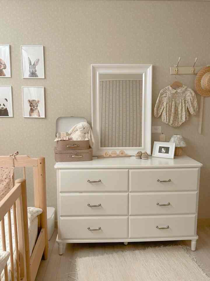 Beige and white toned baby room featuring a white dresser, wooden crib, and animal posters creating a cozy atmosphere