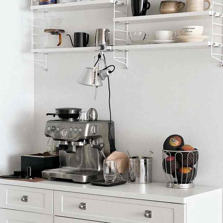 白を基調としたキッチン空間にブレヴィルのコーヒーマシンとストリング棚が配された、清潔でモダンなおうちカフェのインテリア