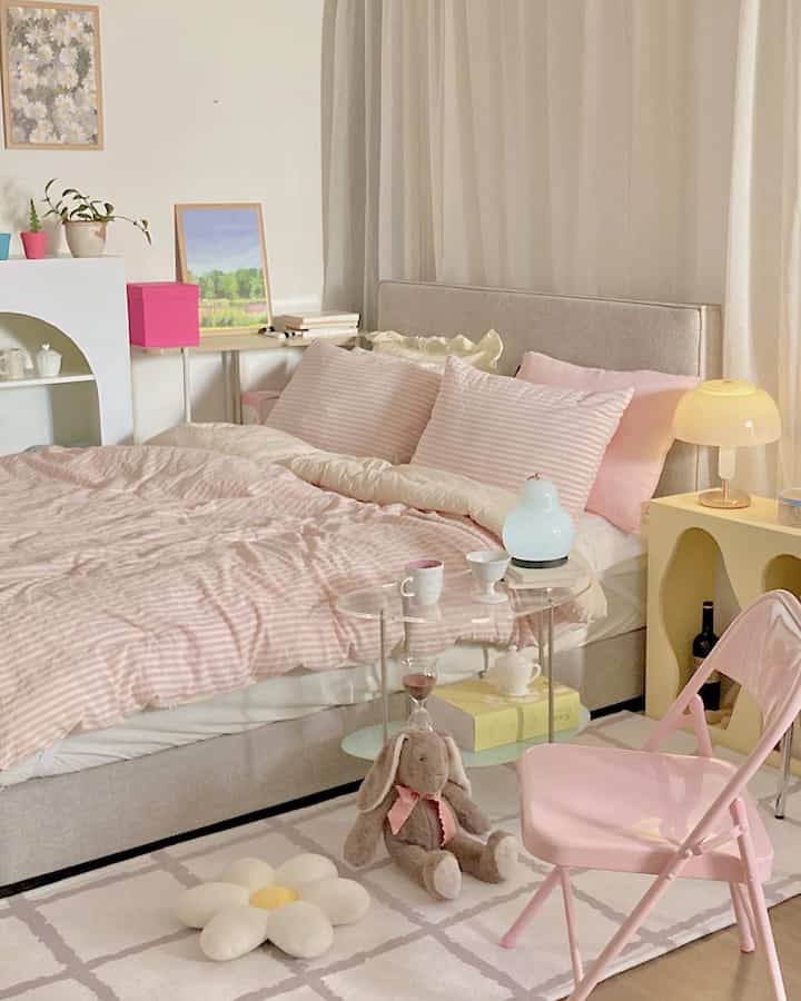 Ivory and pink toned bedroom featuring a large central bed, nightstand, and pink folding chair creating a cozy atmosphere