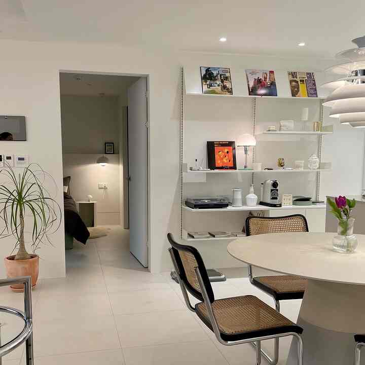 明るいベージュのタイル床と白い壁が調和したモダンなキッチンスペース、ラタン素材のダイニングチェアと丸いテーブルが配置され、落ち着いた雰囲気のインテリア