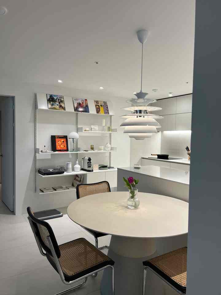 Modern kitchen and dining room in white and wood tones, featuring rattan chairs and a round dining table in a cozy setting