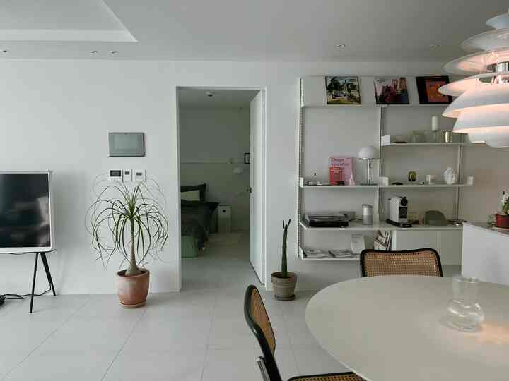 白とベージュのトーンのリビングとキッチン空間、丸いダイニングテーブルとラタンのダイニングチェアが配置されたミニマルなインテリア