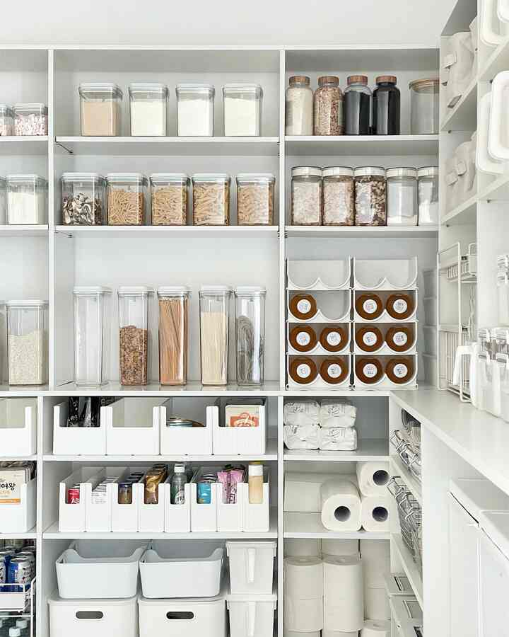 White-toned pantry space featuring transparent storage containers neatly organizing food and household goods with a modern storage vibe