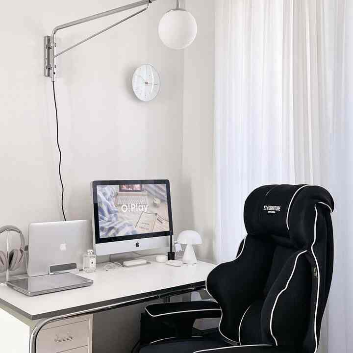 White-toned study space featuring a clean desk with monitor and a black EX Furniture gaming chair, showcasing a simple home office interior
