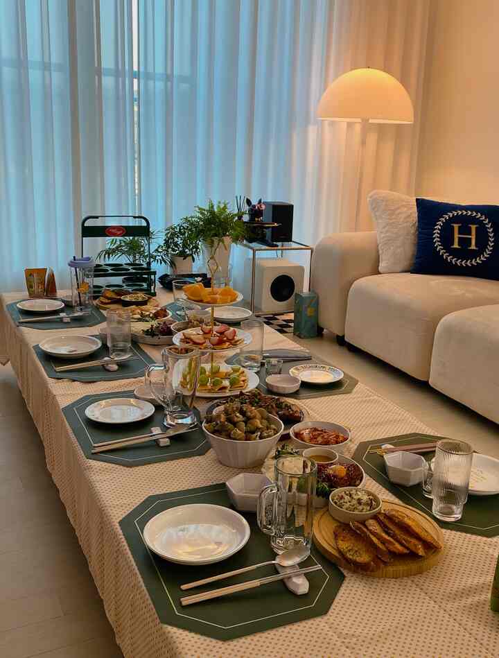 White and beige toned dining room with a long table set for a home party featuring various dishes and cozy atmosphere