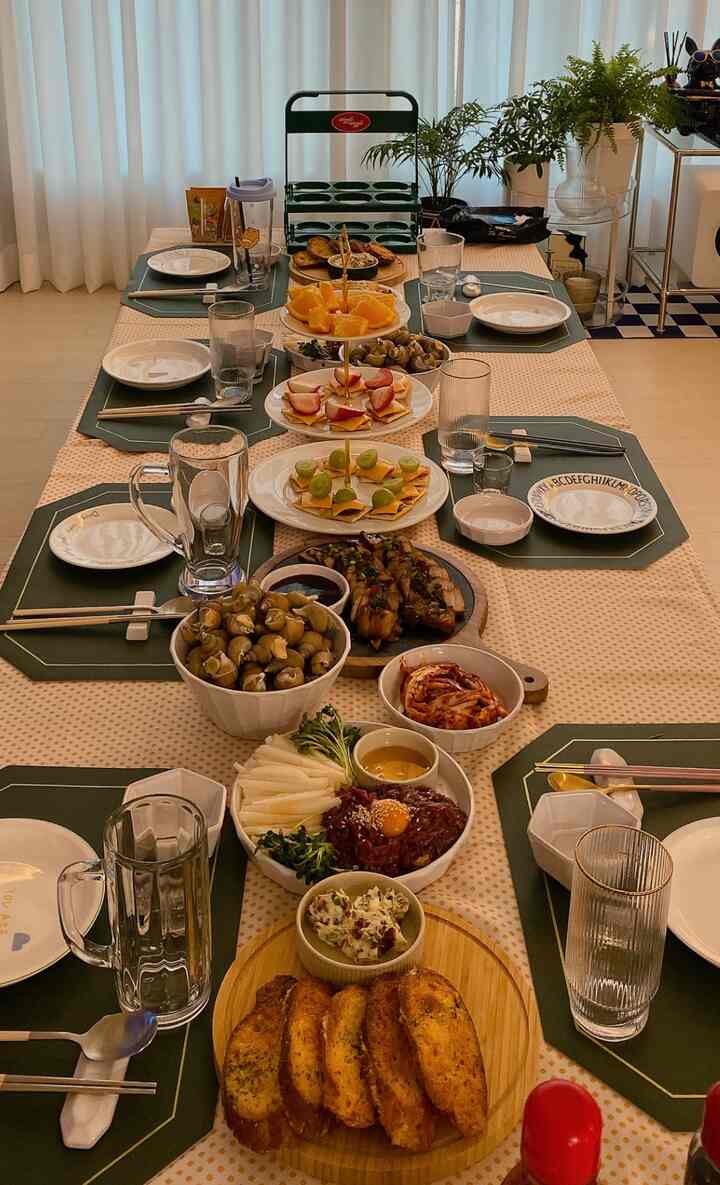 ベージュのドットテーブルクロスと緑のランチョンマットが敷かれたダイニング、様々な料理とトレイが並ぶ雰囲気のあるホームパーティー空間