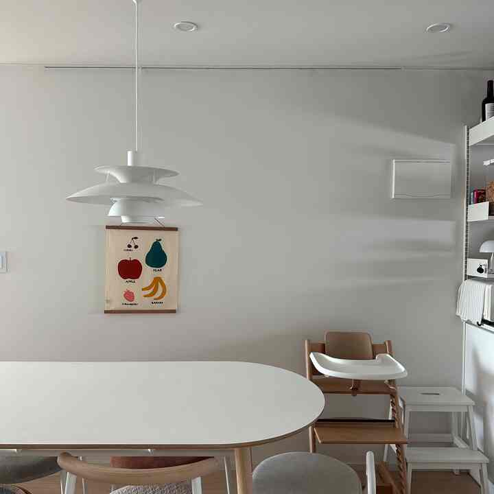 White and natural tone dining room featuring a baby high chair and pendant light, creating a clean and cozy atmosphere