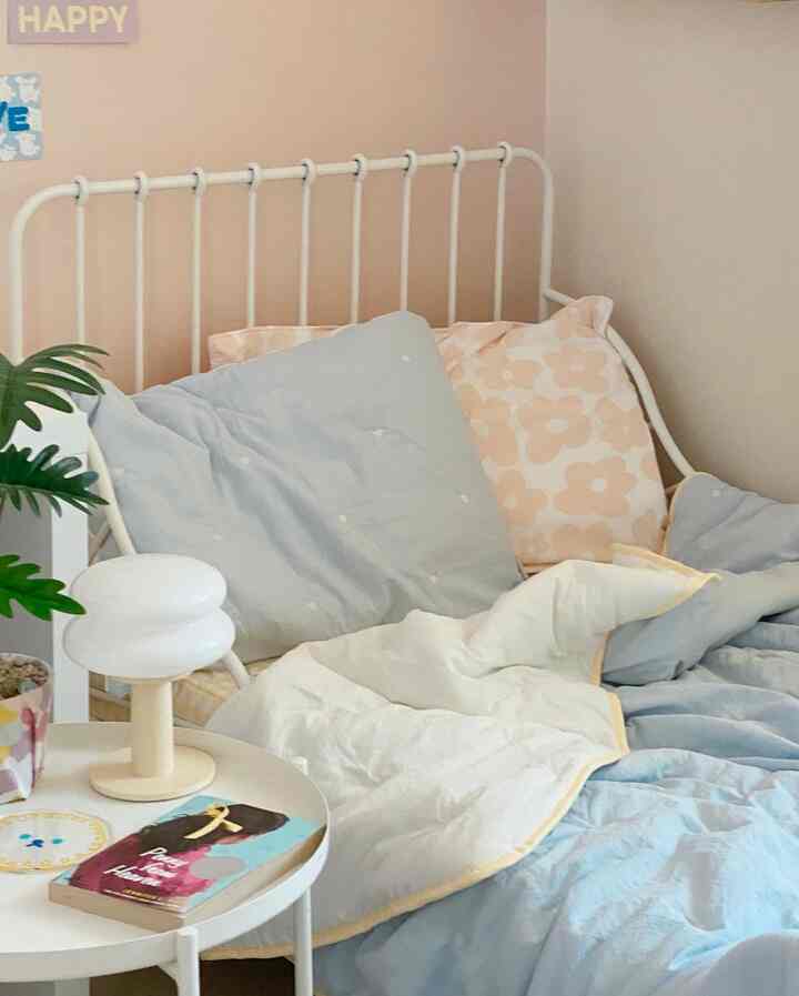 Pastel-toned kids' room featuring a bed with pillows and bedding, white side table holding a lamp and book