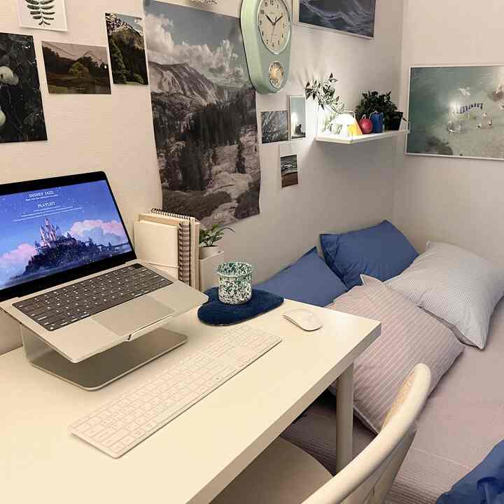A cozy small bedroom in white and blue tones featuring a desk with computer and cushions