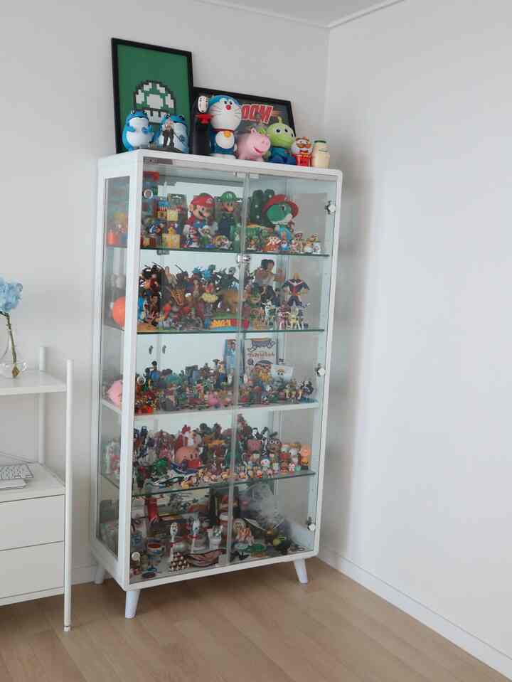 White-toned room featuring glass cabinet filled with diverse character figures, creating a clean hobby room atmosphere