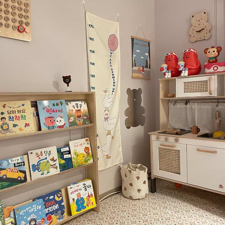 ナチュラルな木目調とパステルカラーが調和した子供部屋、低い本棚や身長計、木製のキッチンおもちゃが配置された温かみのあるインテリア