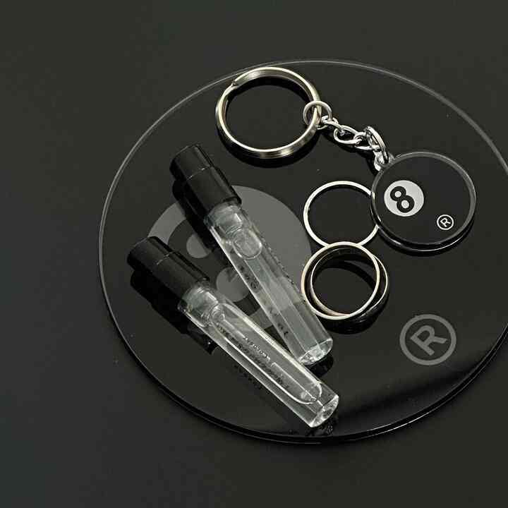 A sleek accessory image showing keyrings and perfume vials on a black monotone circular tray