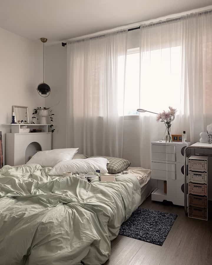 明るい白を基調とした寝室、ミントグリーンの寝具と自然光が透けるカーテン、ミニマルなインテリアが調和した空間