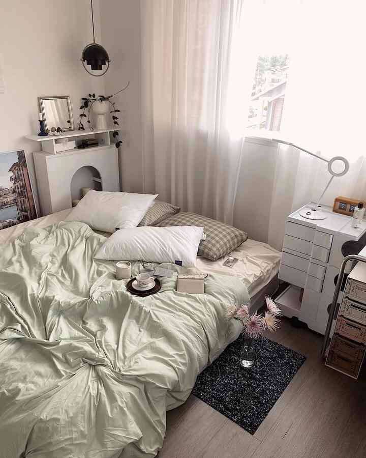 Bright white and light gray toned bedroom featuring a large bed, sheer curtains, and a modern floor lamp creating a cozy atmosphere