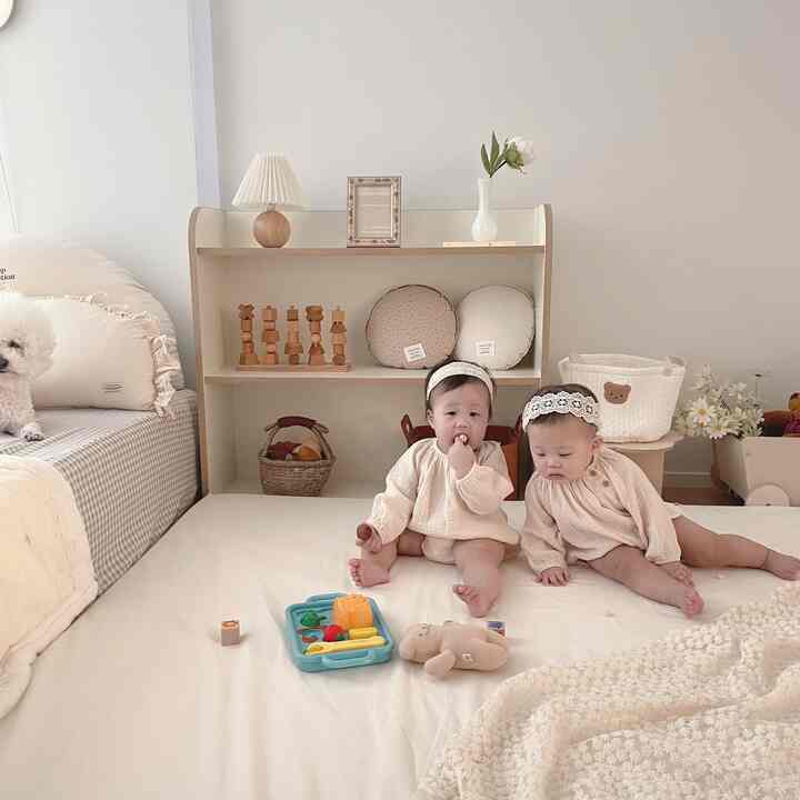 Ivory-toned baby room featuring wooden toy shelves and two babies seated on a mat, creating a warm and tidy atmosphere