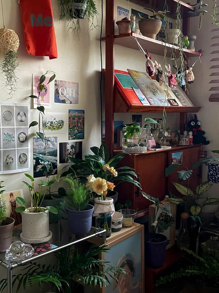 Small room interior featuring wood tones and abundant green plants, decorated with wall shelves and posters for a warm atmosphere