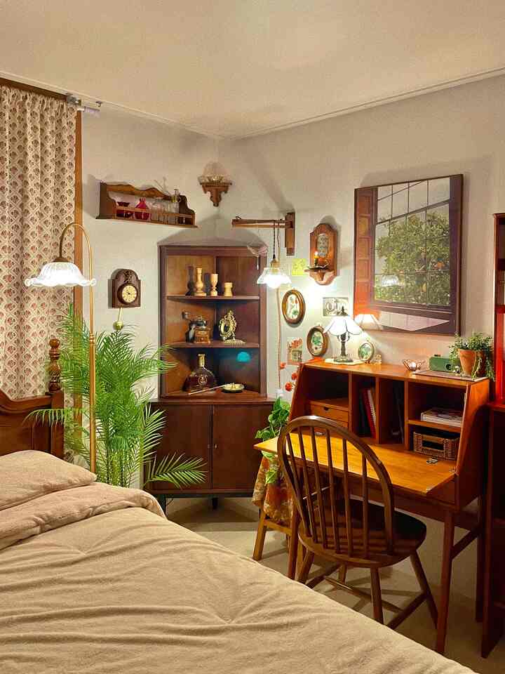 Natural beige and wood-toned bedroom featuring vintage decor, wall sconces, corner cabinet, and a wooden desk creating a cozy atmosphere