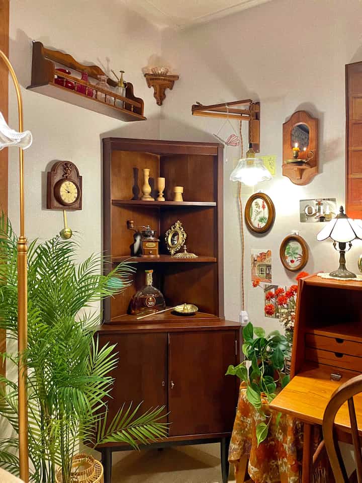 Wood tone vintage living room corner featuring antique clock, wall sconces, and lush green plants with warm ambiance